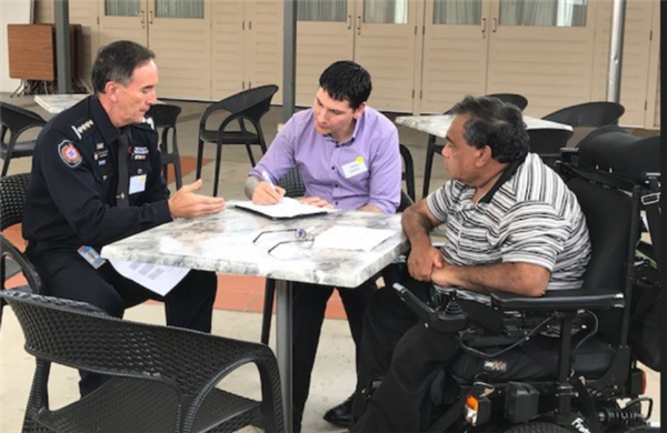 Photo of three people sat around a table discussing disaster preparedness. One man is in a wheelchair, another is sat in a chair, and third is wearing a QFES uniform