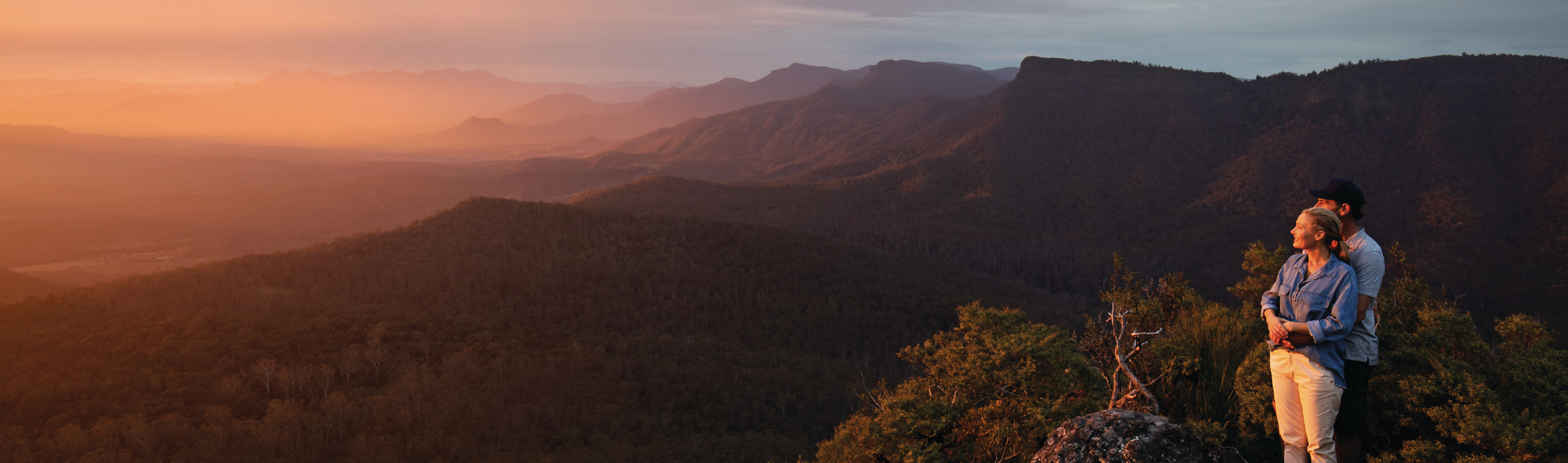 a couple standing on a mountain overlooking an orange sunset