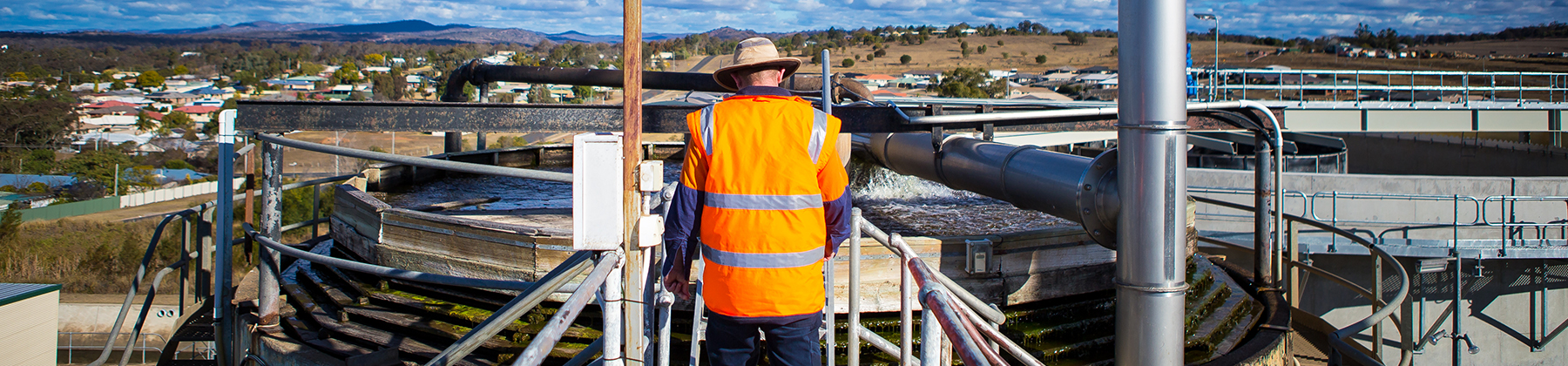 Landing Page_Water and Wastewater showing a Council officer in a high-viz workwear walking across the metal bridge of a water treatment plant to inspect the infrastructure.